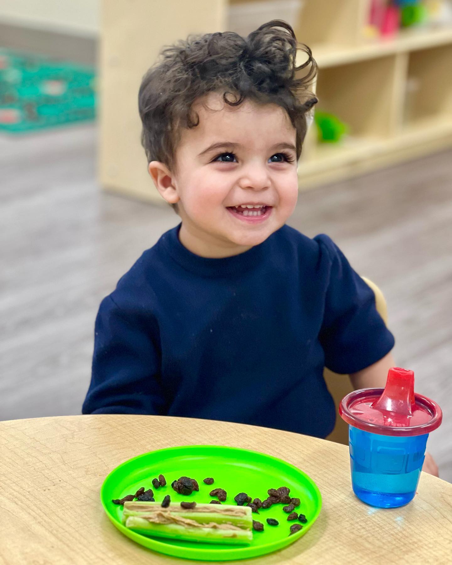 smiling toddler boy eating ants on a log snack at preschool