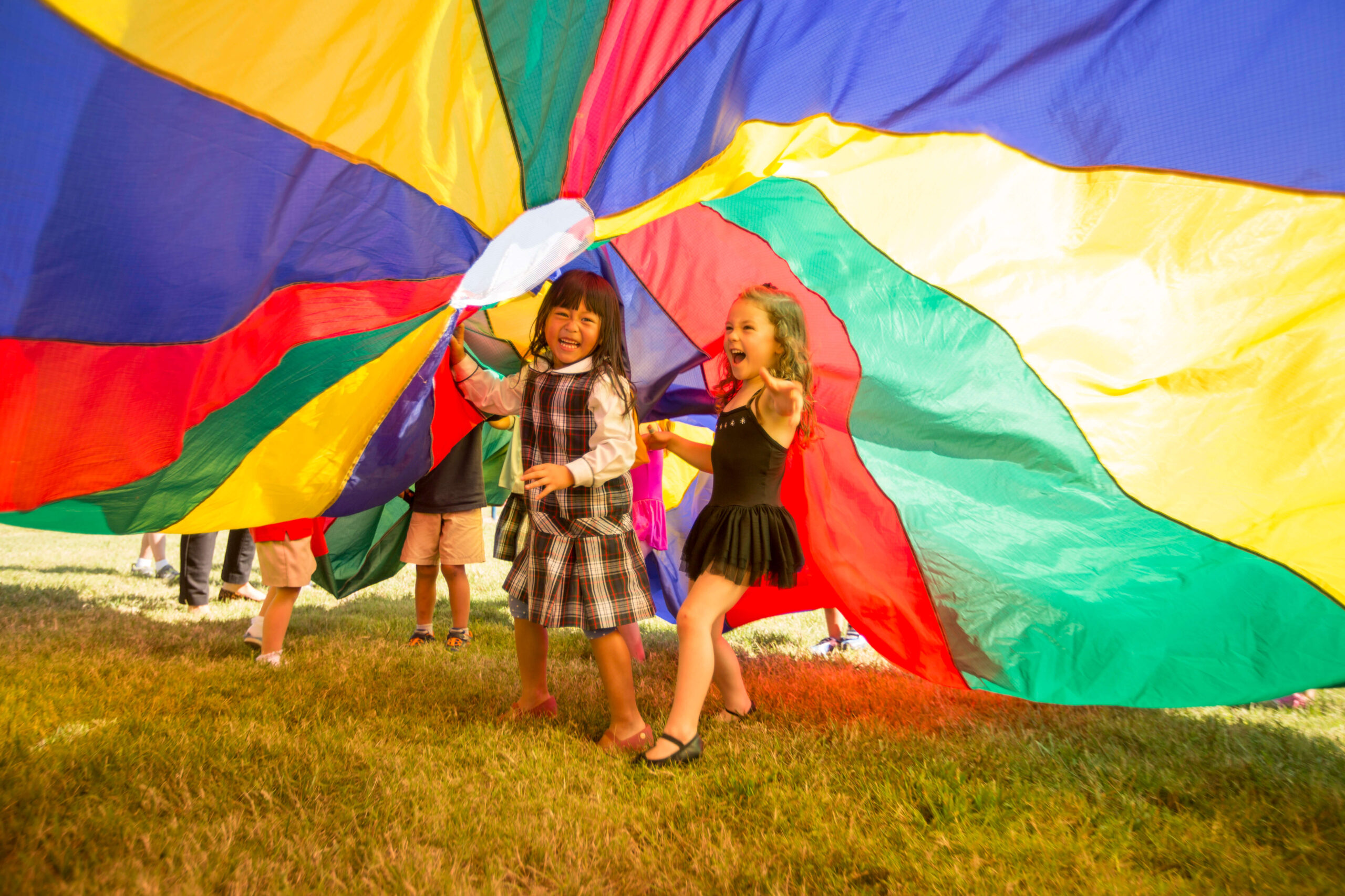 children running under rainbow parachute
