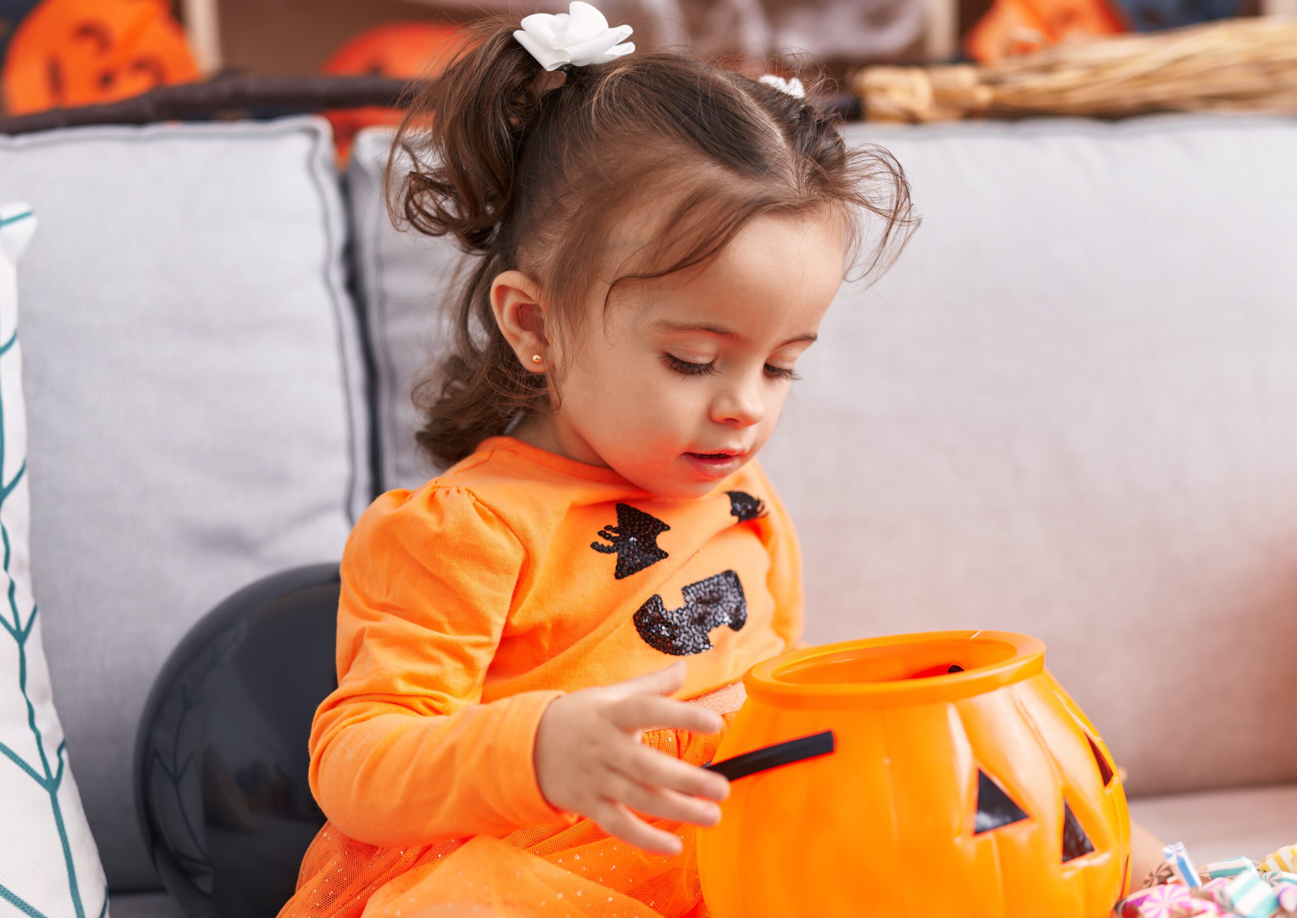 preschool-age child in pumpkin dress looking into her halloween candy bucket