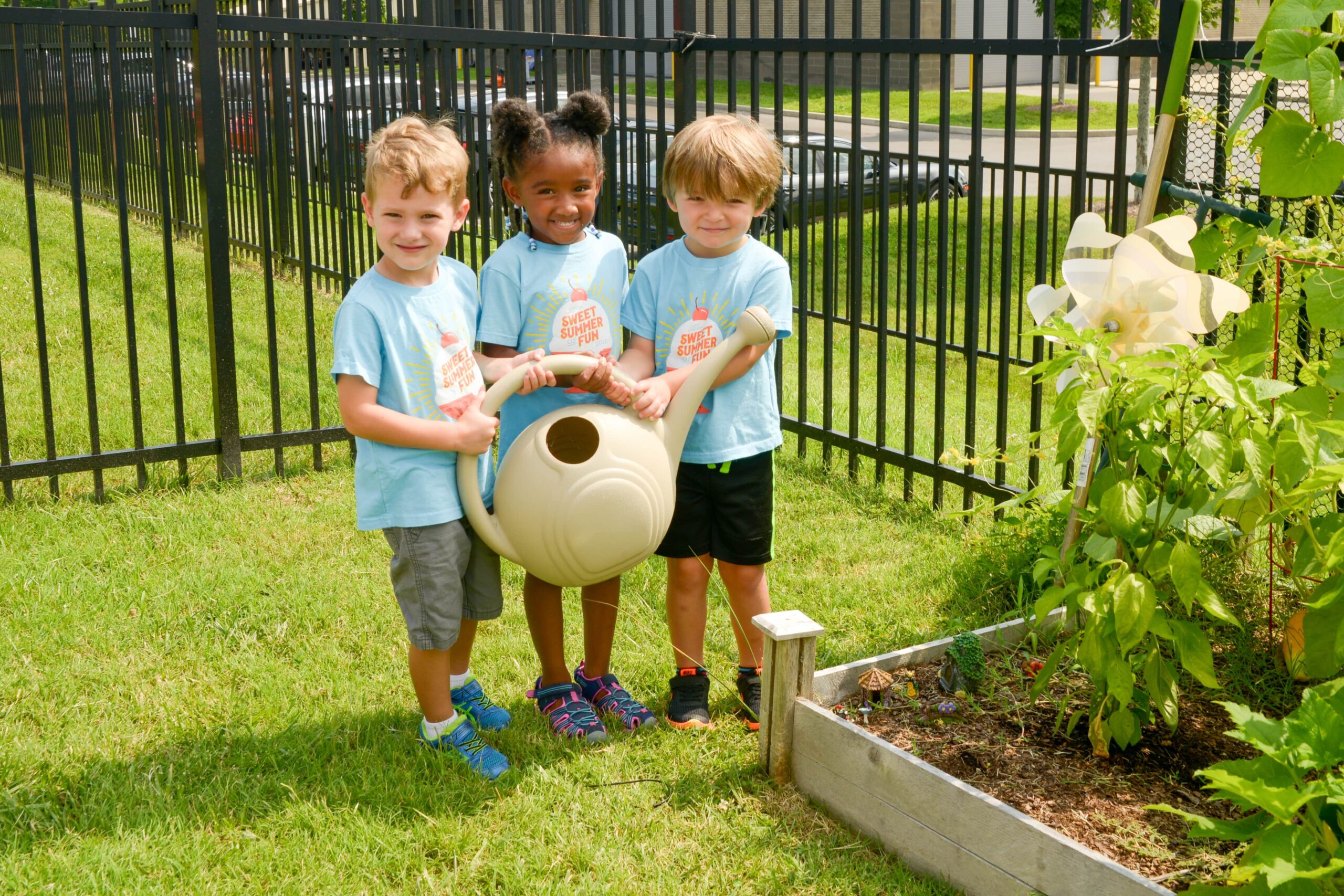 three preschoolers holding watering jug near garden