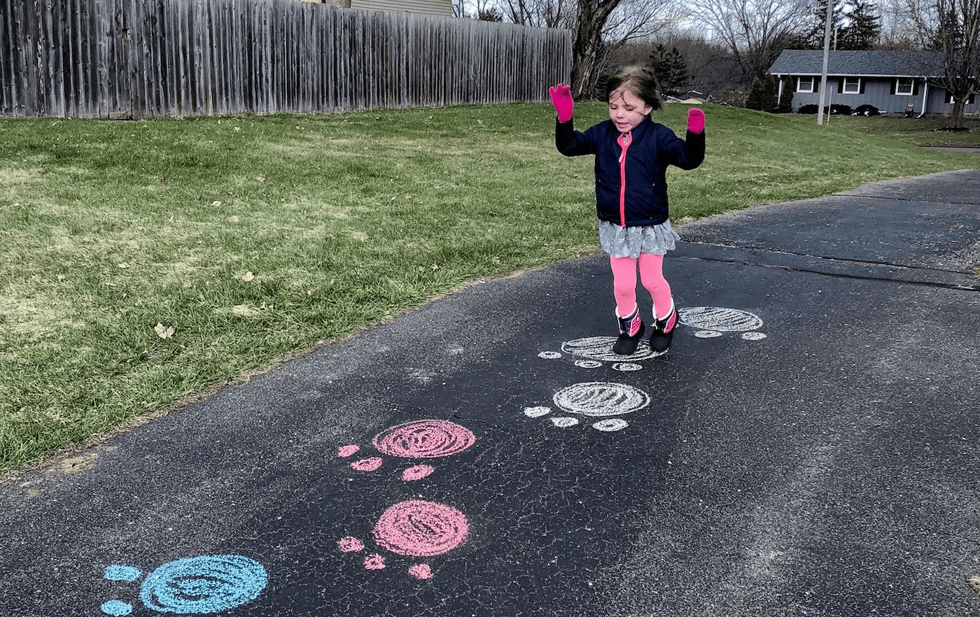 child playing hopscotch on black pavement