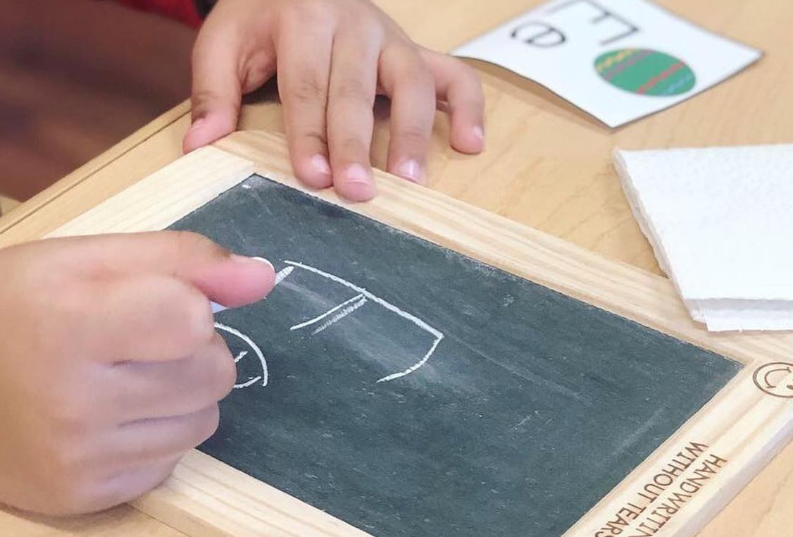 person writing a capital and lower case "e" on a personal chalkboard at home