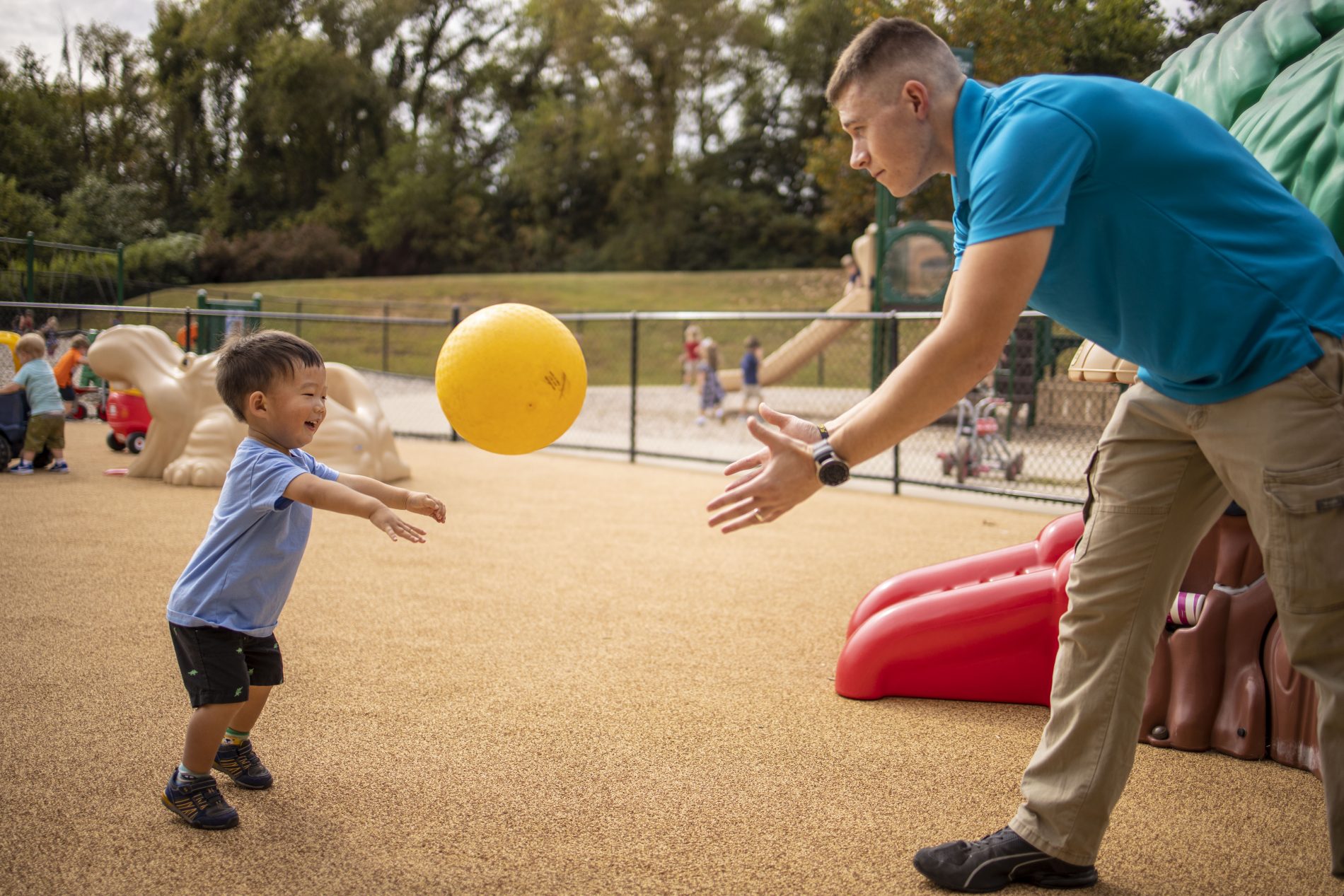 teacher and child on playground playing catch with yellow ball