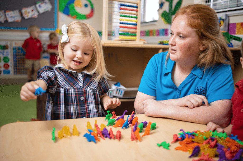 preschool teacher and girl playing with dinosaur toys