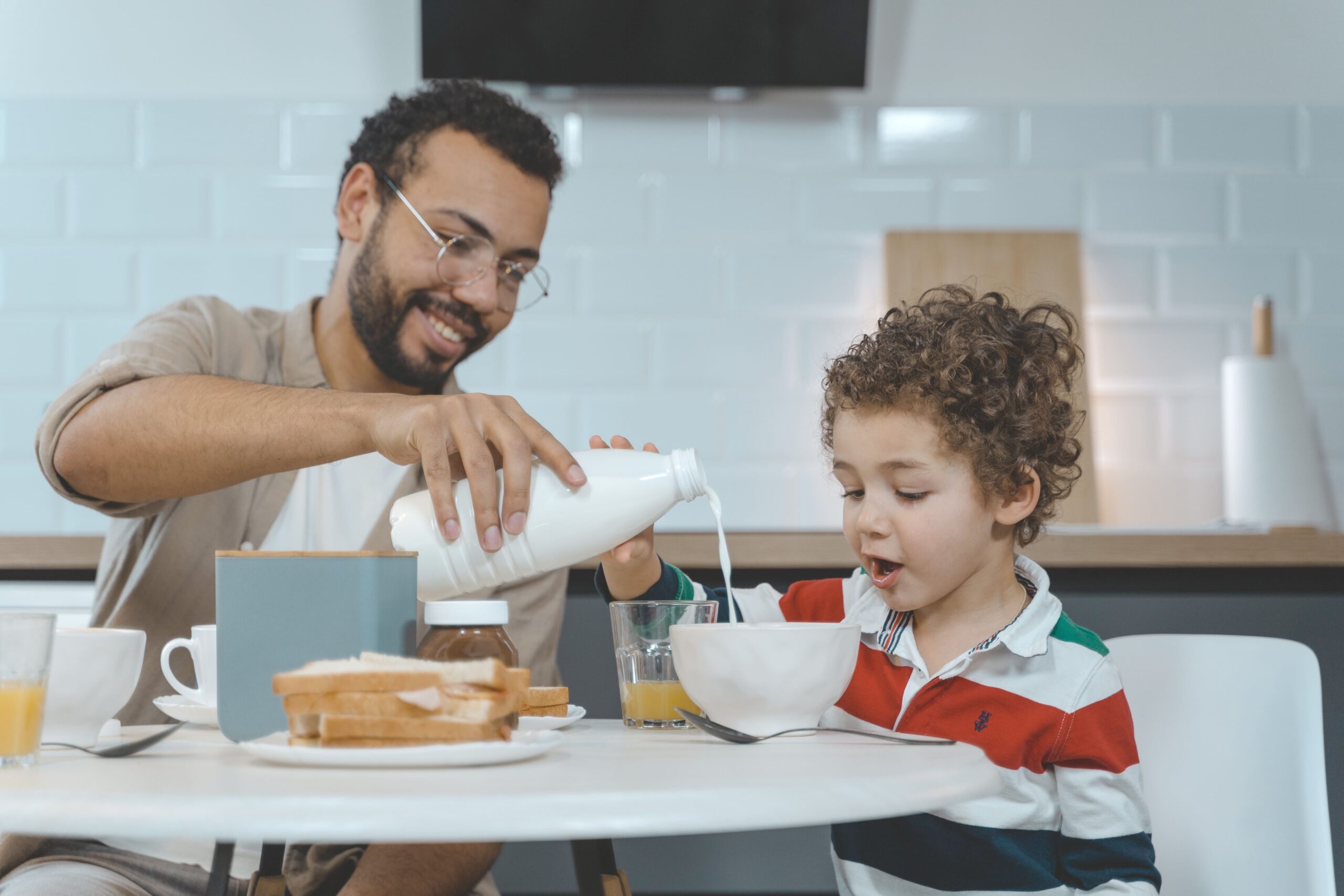 dad pouring milk over toddler's cereal