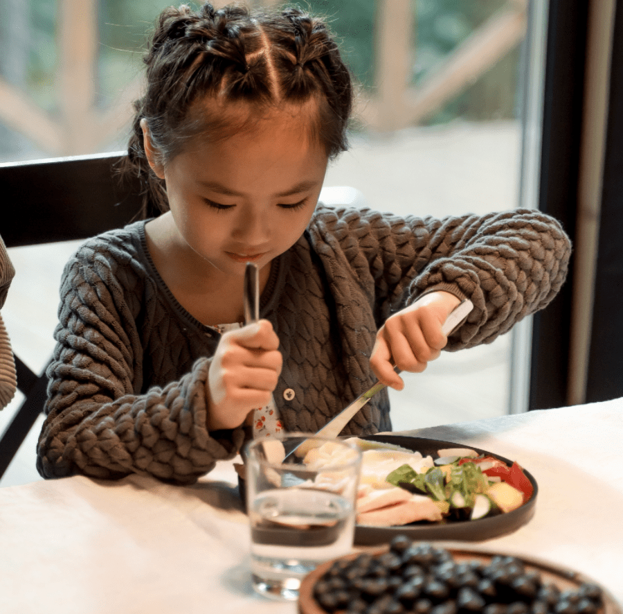 girl cutting up food at table
