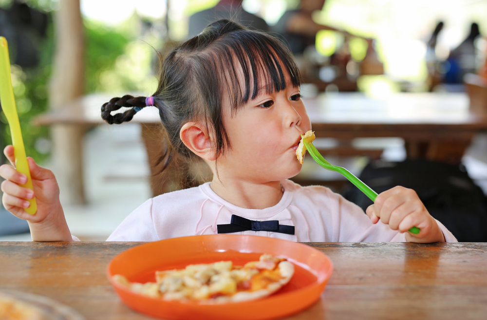 little girl eating with utensils