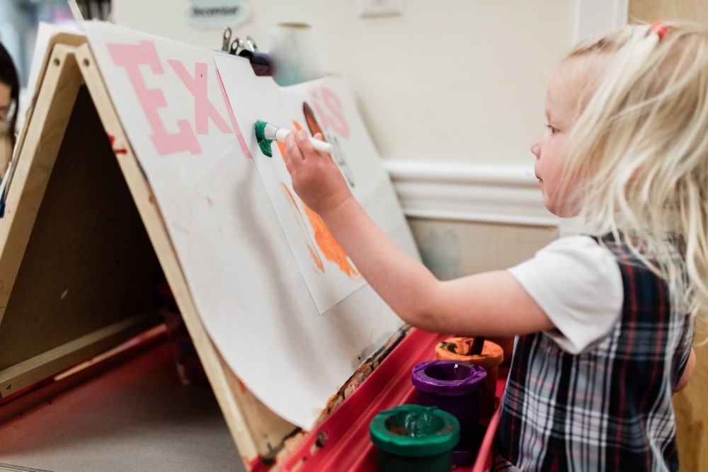 preschool student girl painting on easel in classroom