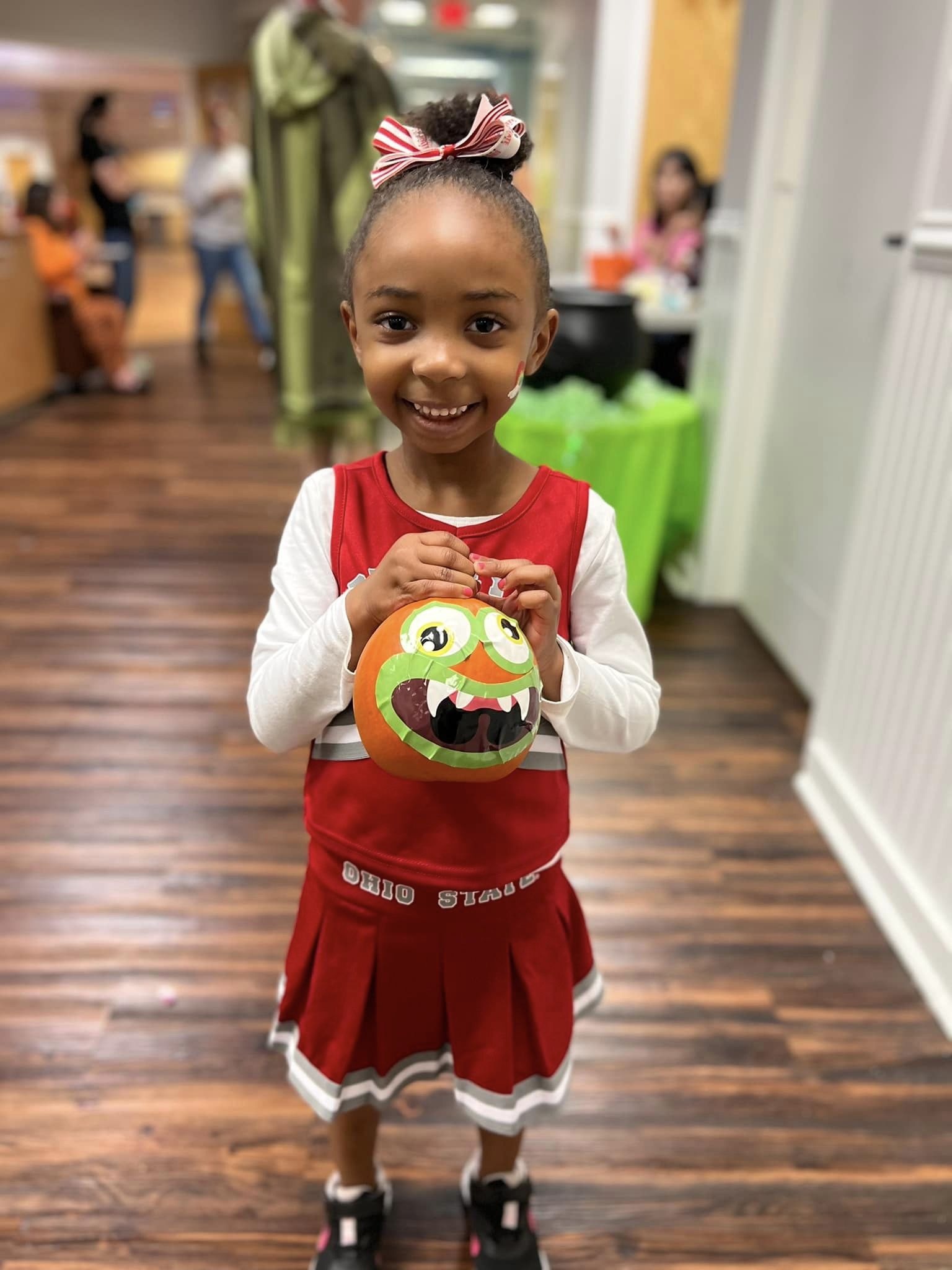 little girl smiling holding a painted pumpkin