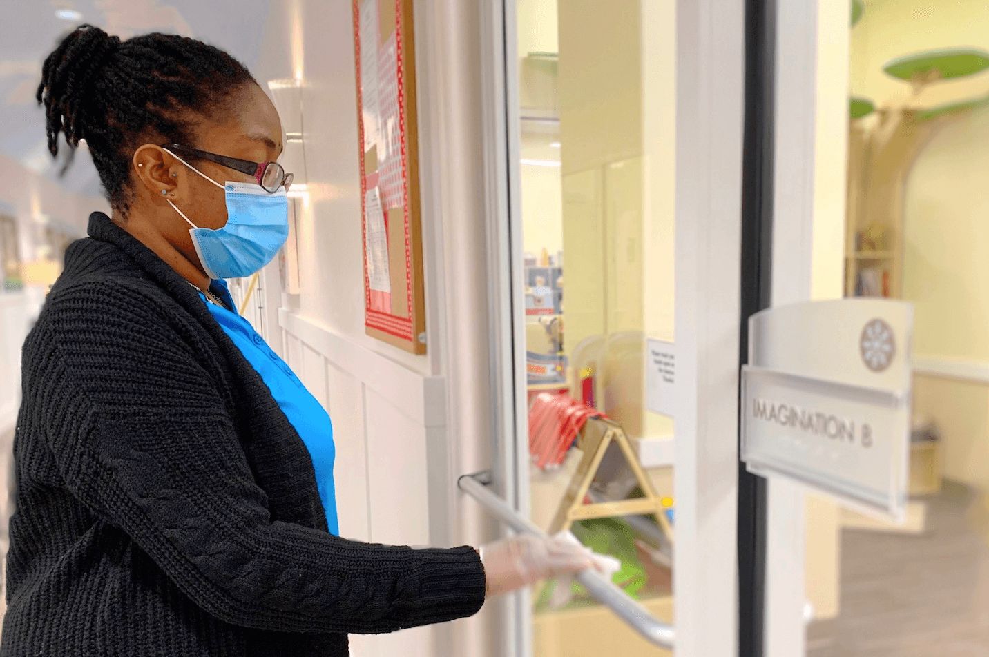 masked preschool teacher cleaning door handle