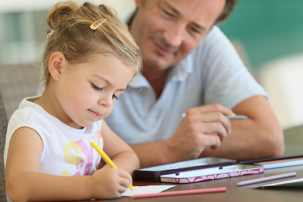 Daddy watching little girl drawing on paper