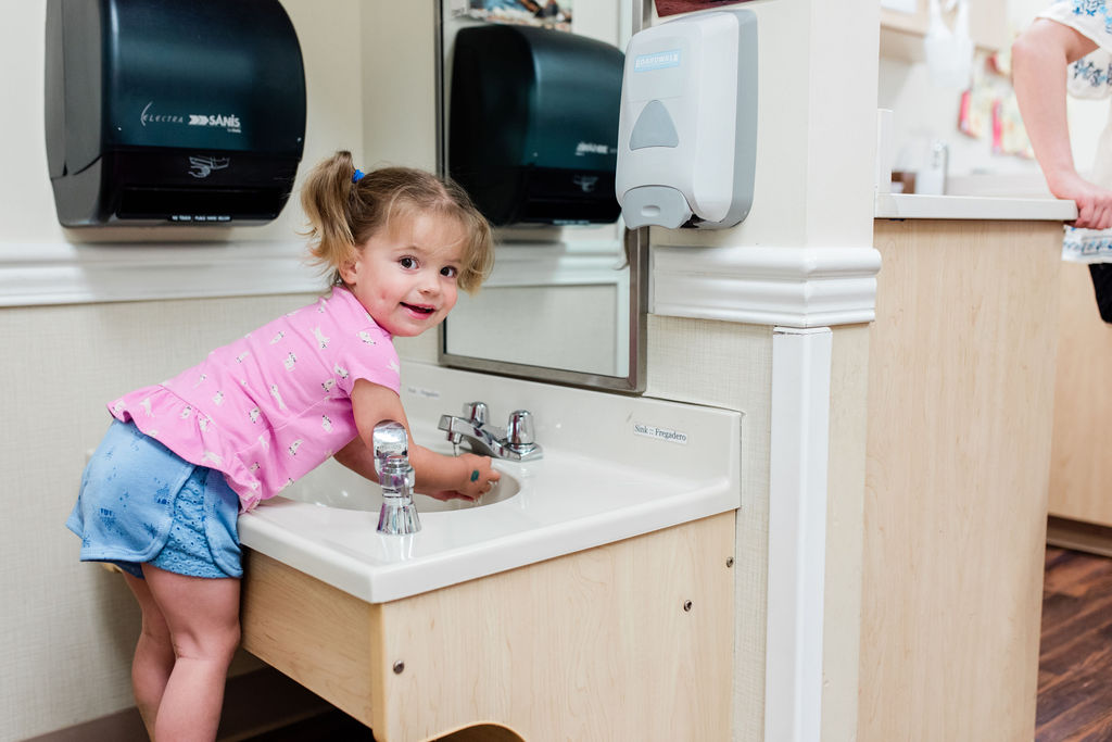 preschooler washing her hands at a bathroom sink