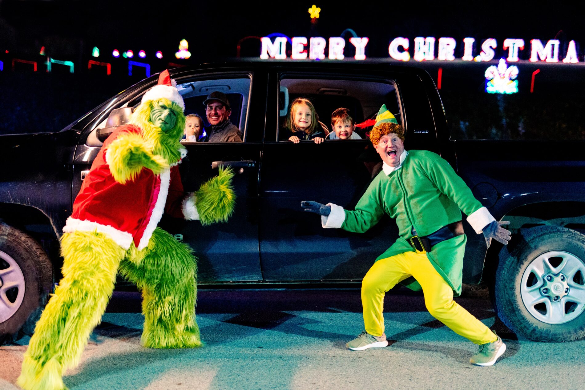 Grinch and Elf characters standing outside a family in their car driving through Festival of Lights