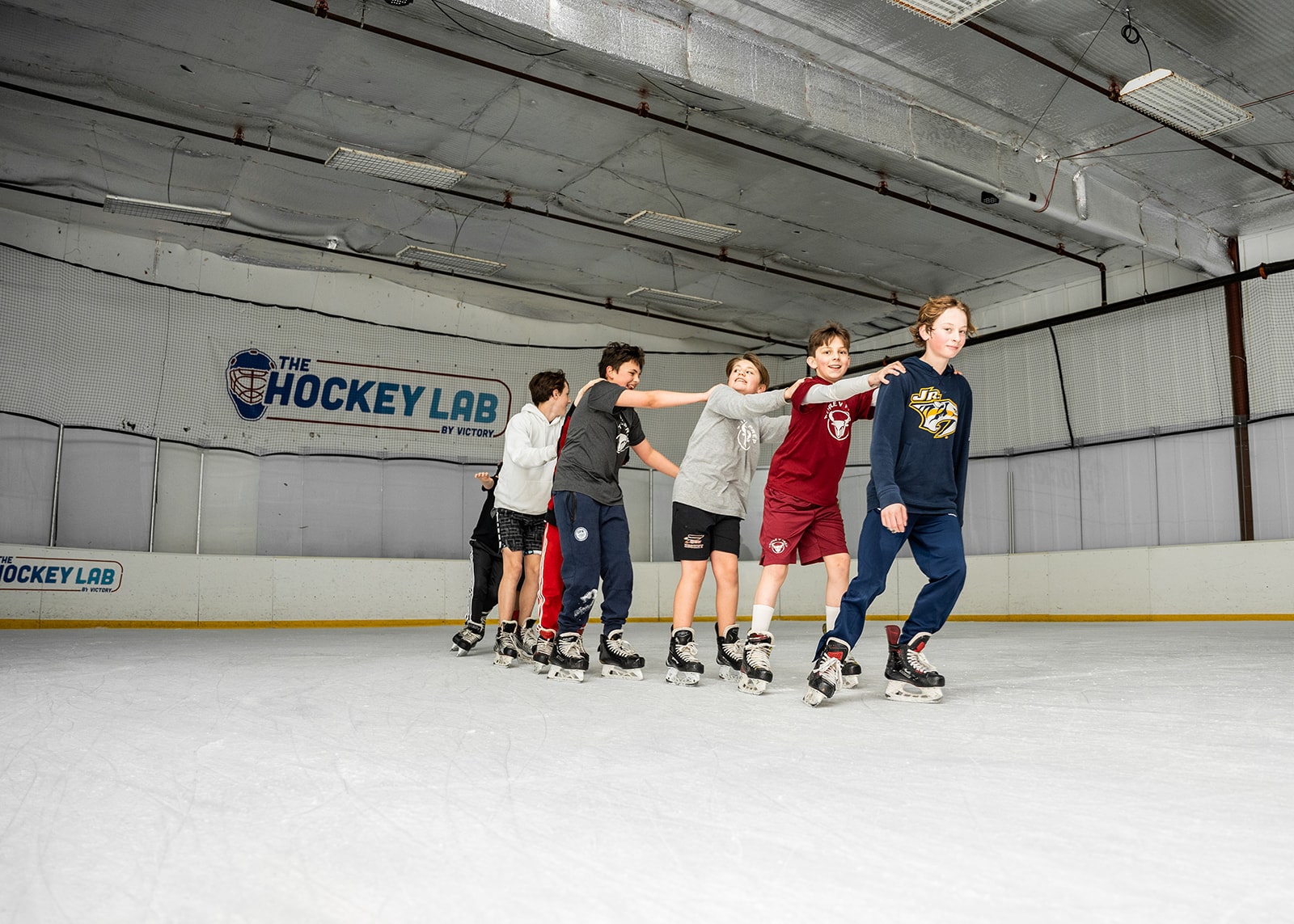 seven kids ice skating in a line on a hockey rink
