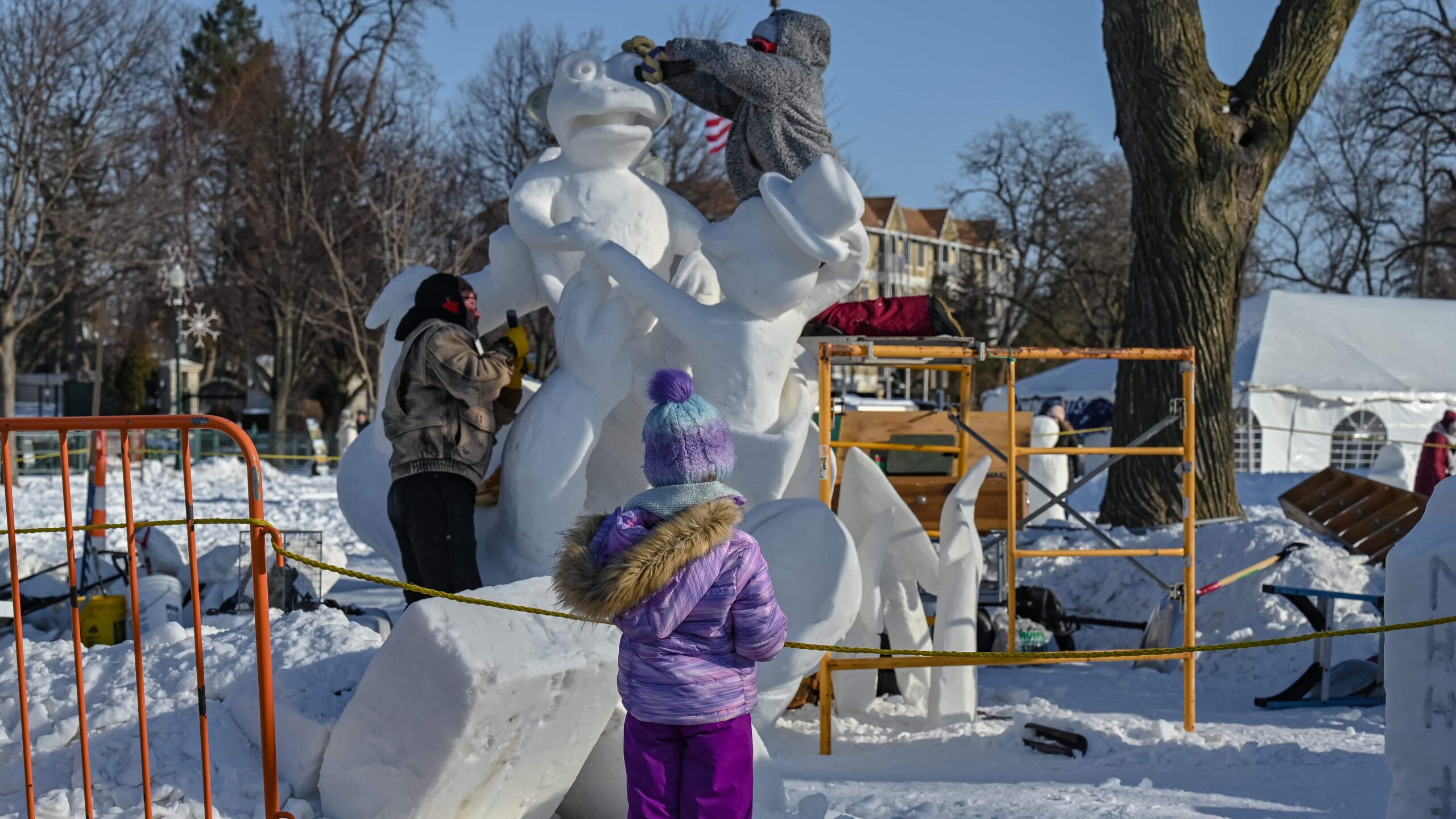 child watches two people working on a snow sculpture at Lake Geneva Winterfest