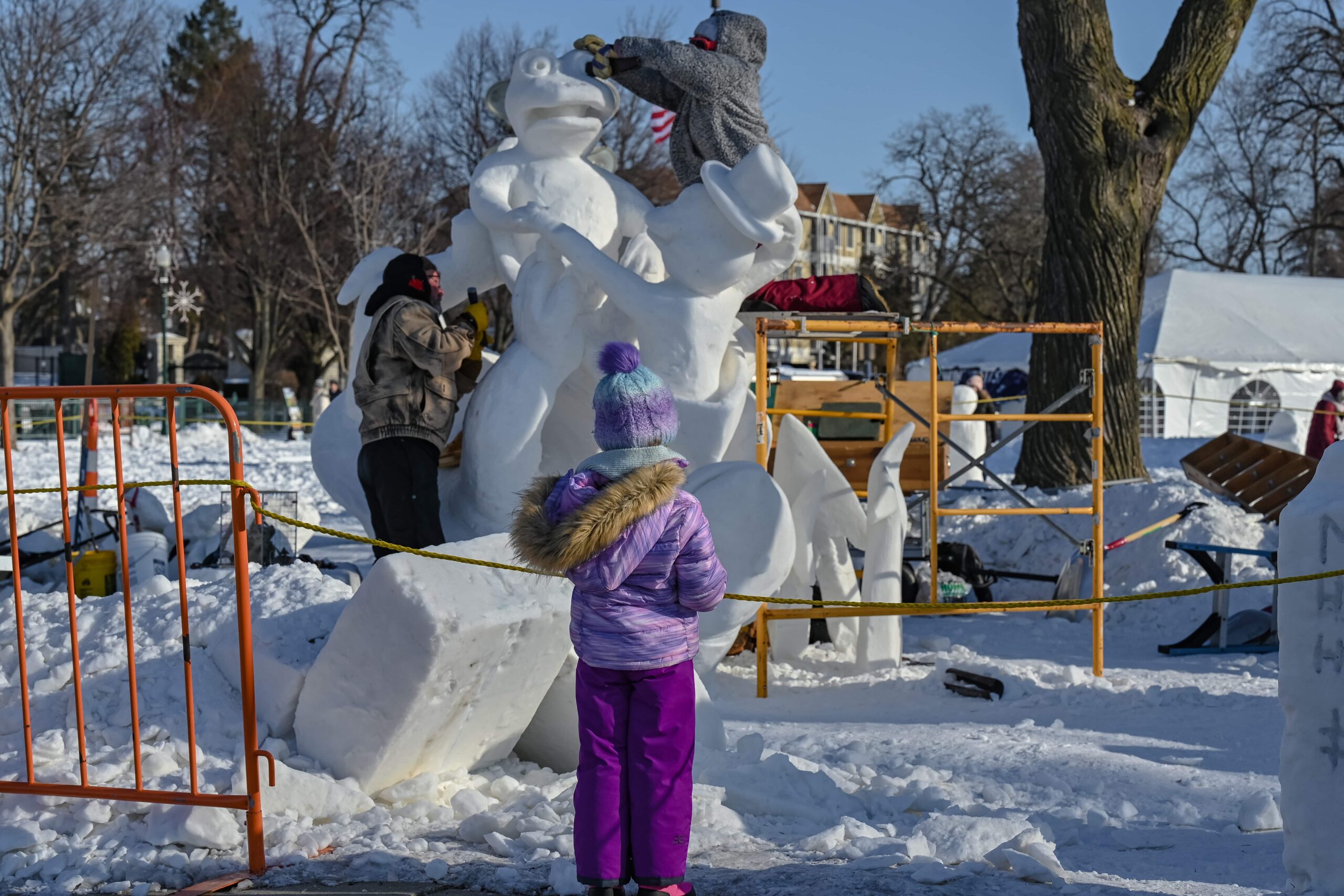 child watches two people working on a snow sculpture at Lake Geneva Winterfest