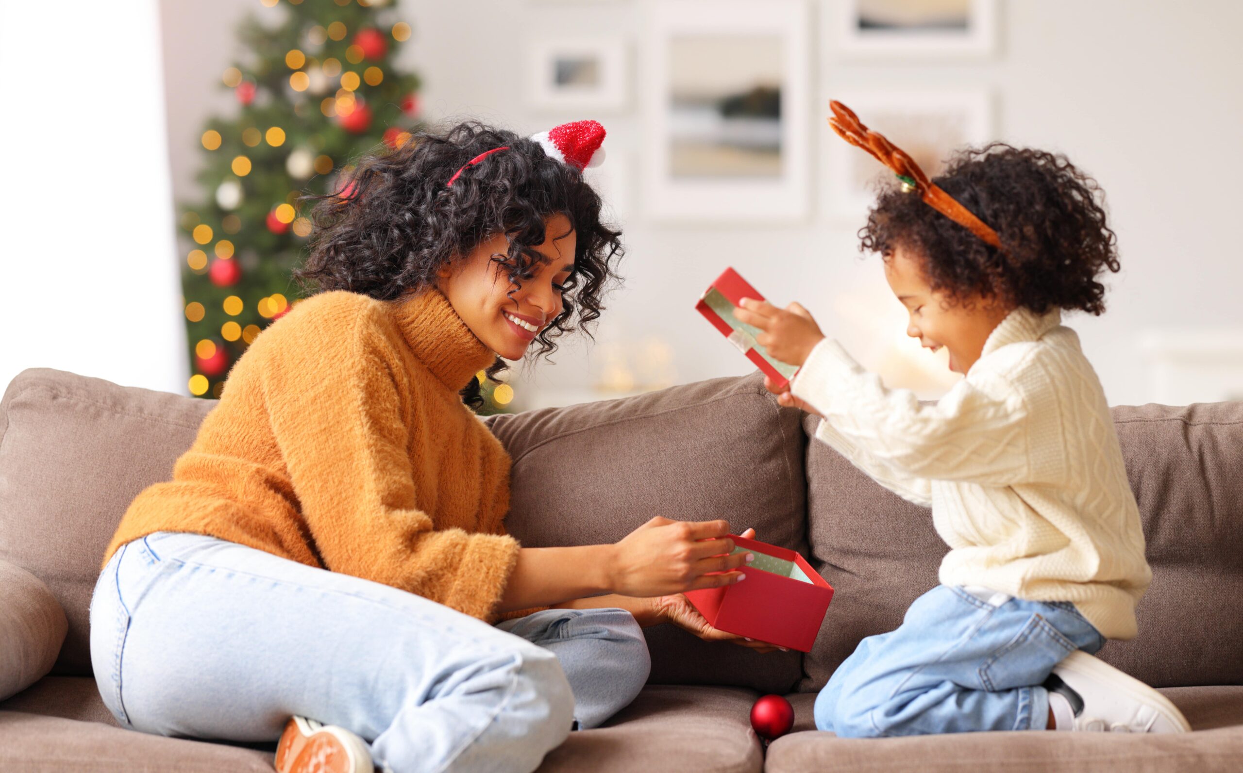mom and preschool age child opening a christmas present on the couch