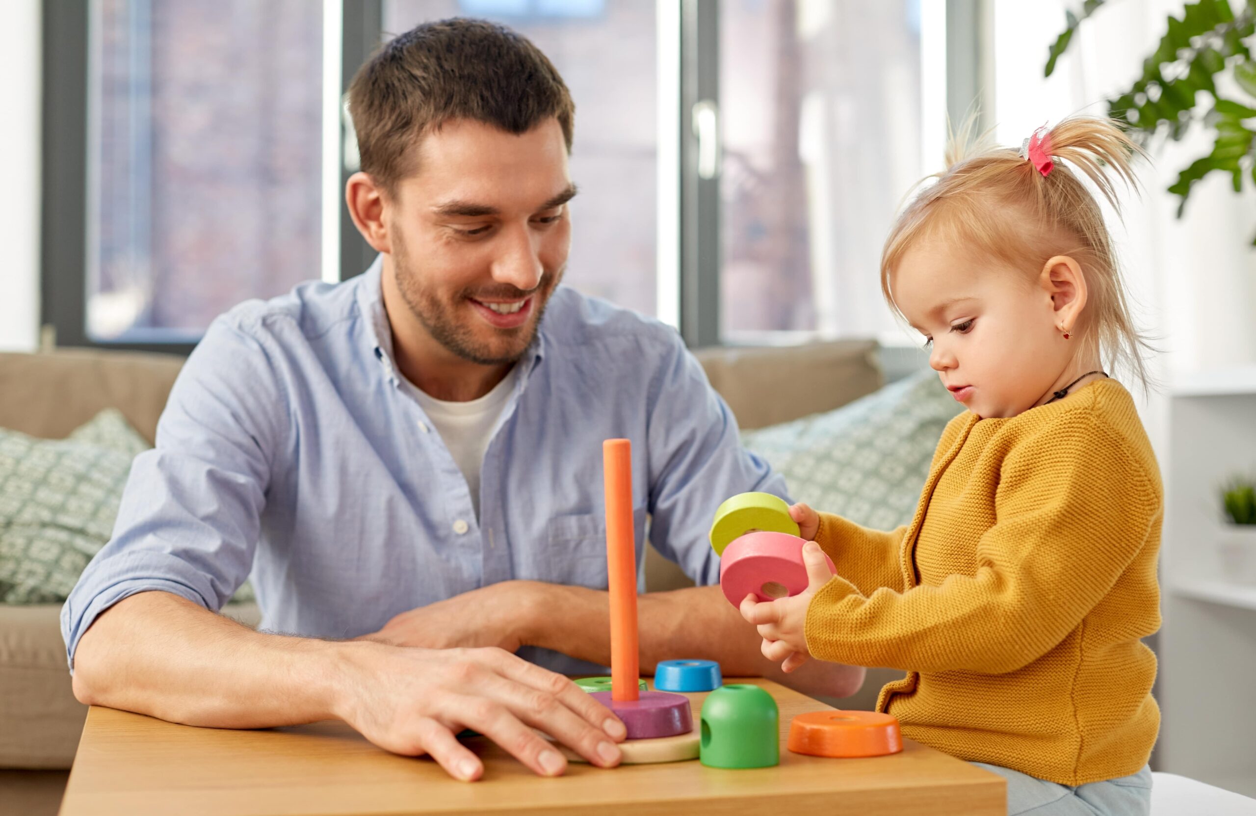 dad helping toddler daughter play with toy rings
