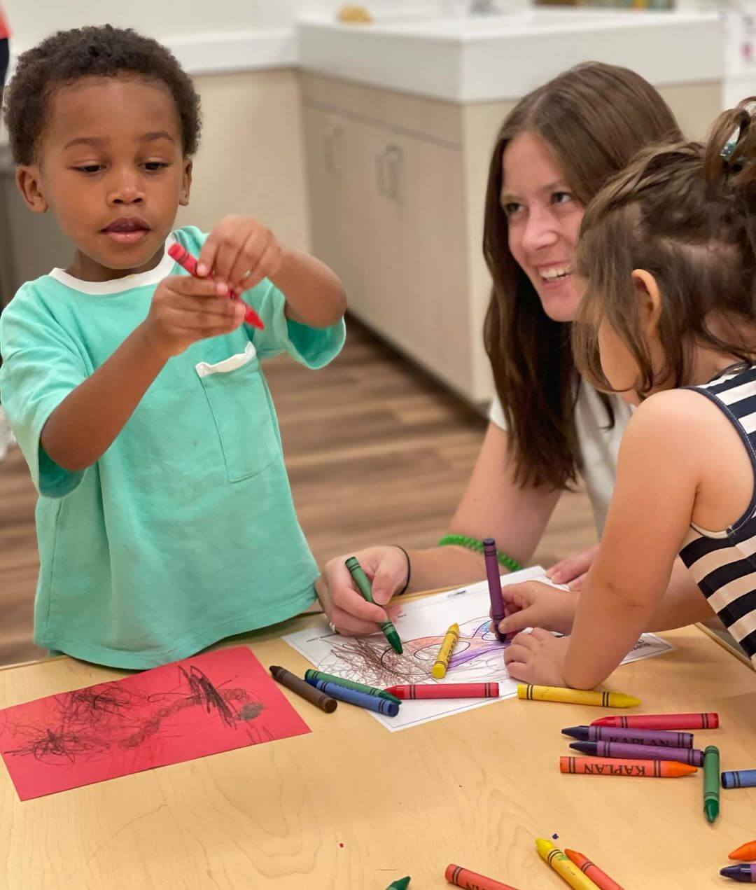 preschool teacher and two preschool students coloring with crayons