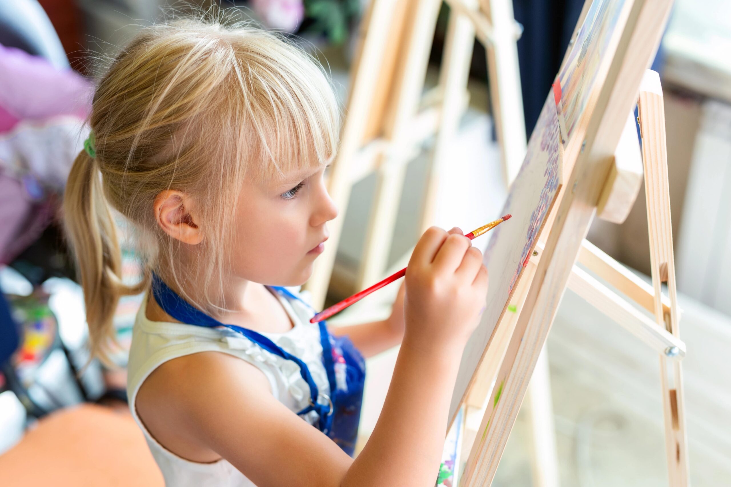 preschool-aged girl painting on an easel