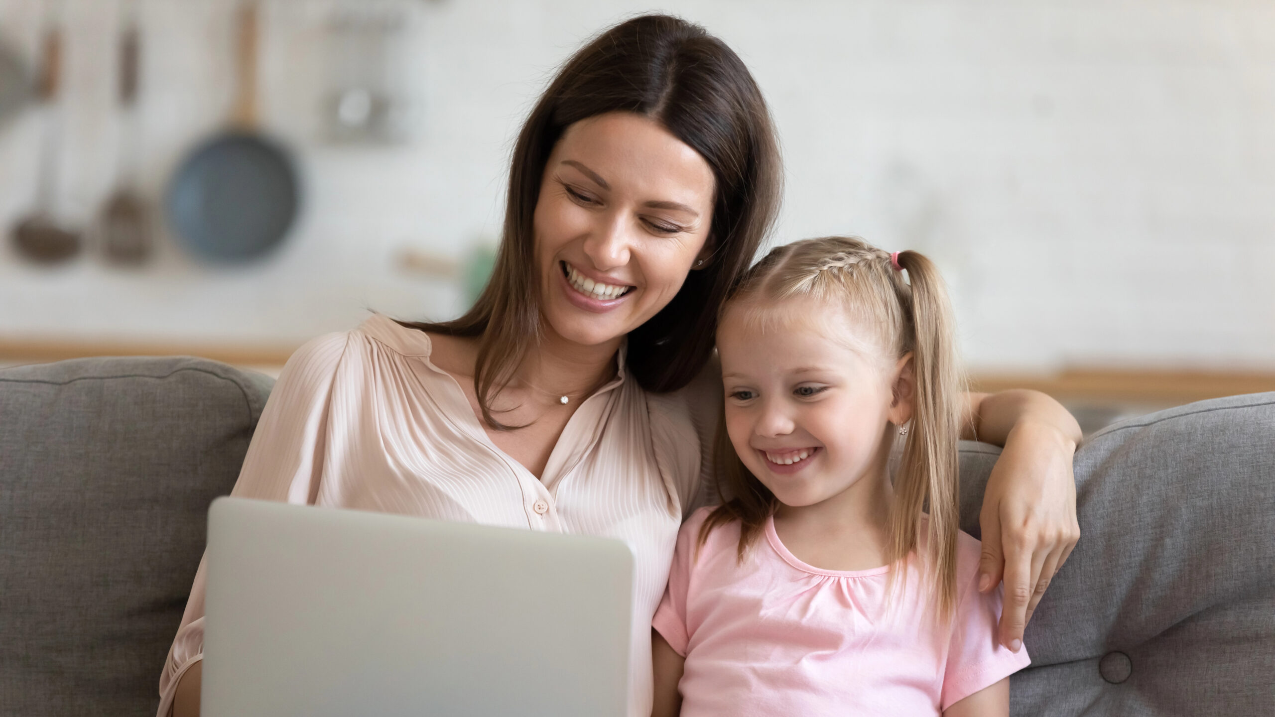 mother and daughter using a laptop together on the couch