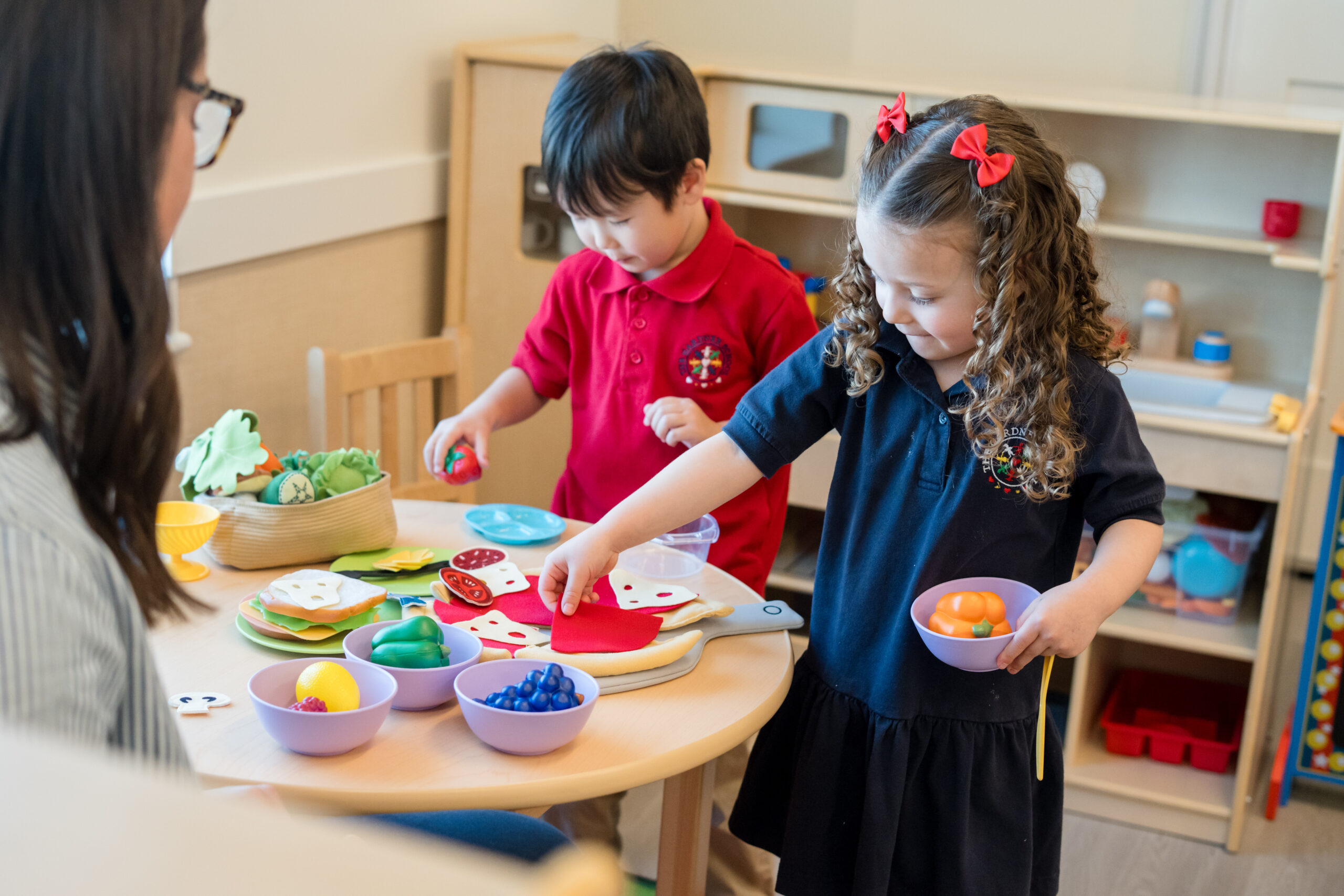 2 children playing in play kitchen with play food.