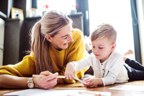 mom smiling at young child while he draws
