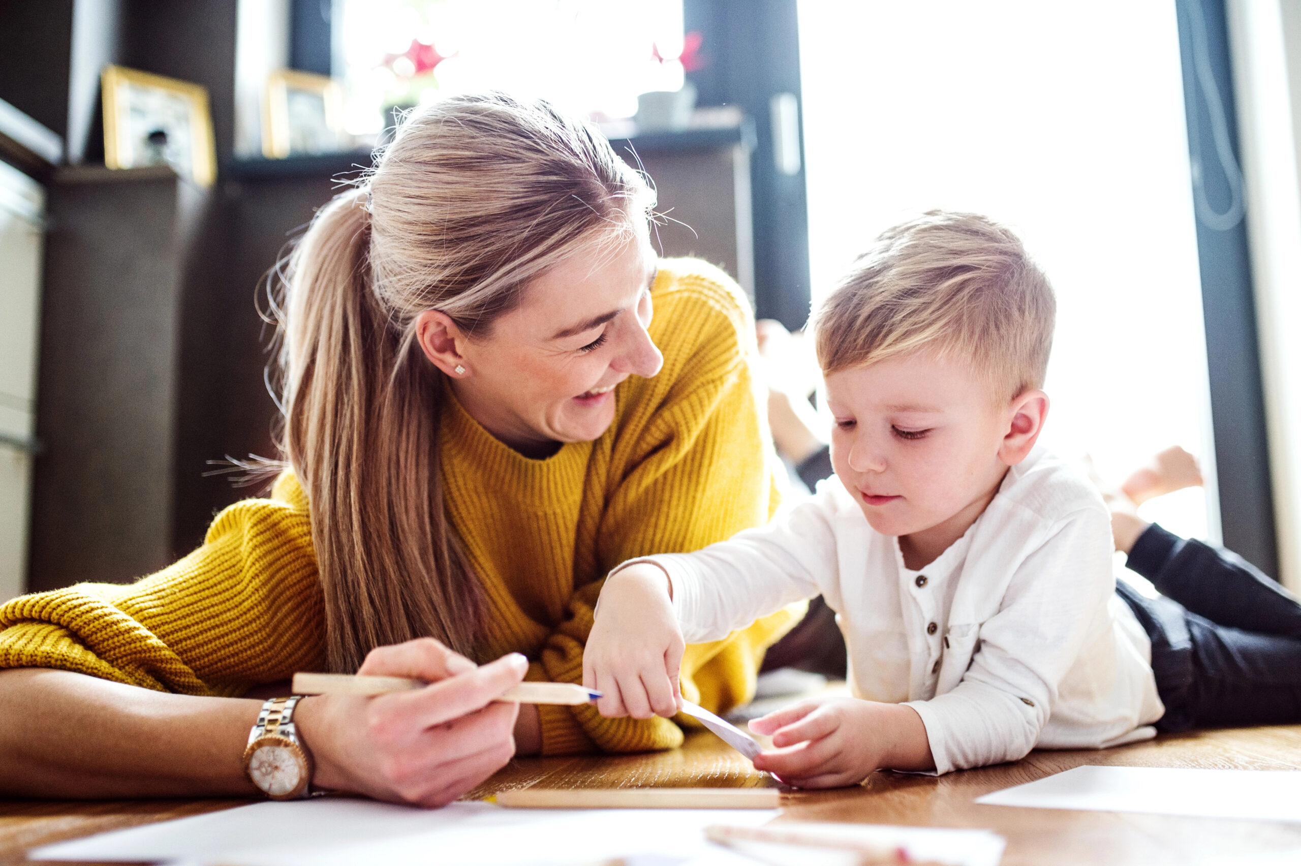 mom smiling at young child while he draws