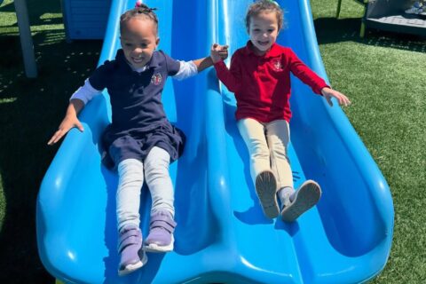 two young female students coming down the slide on playground