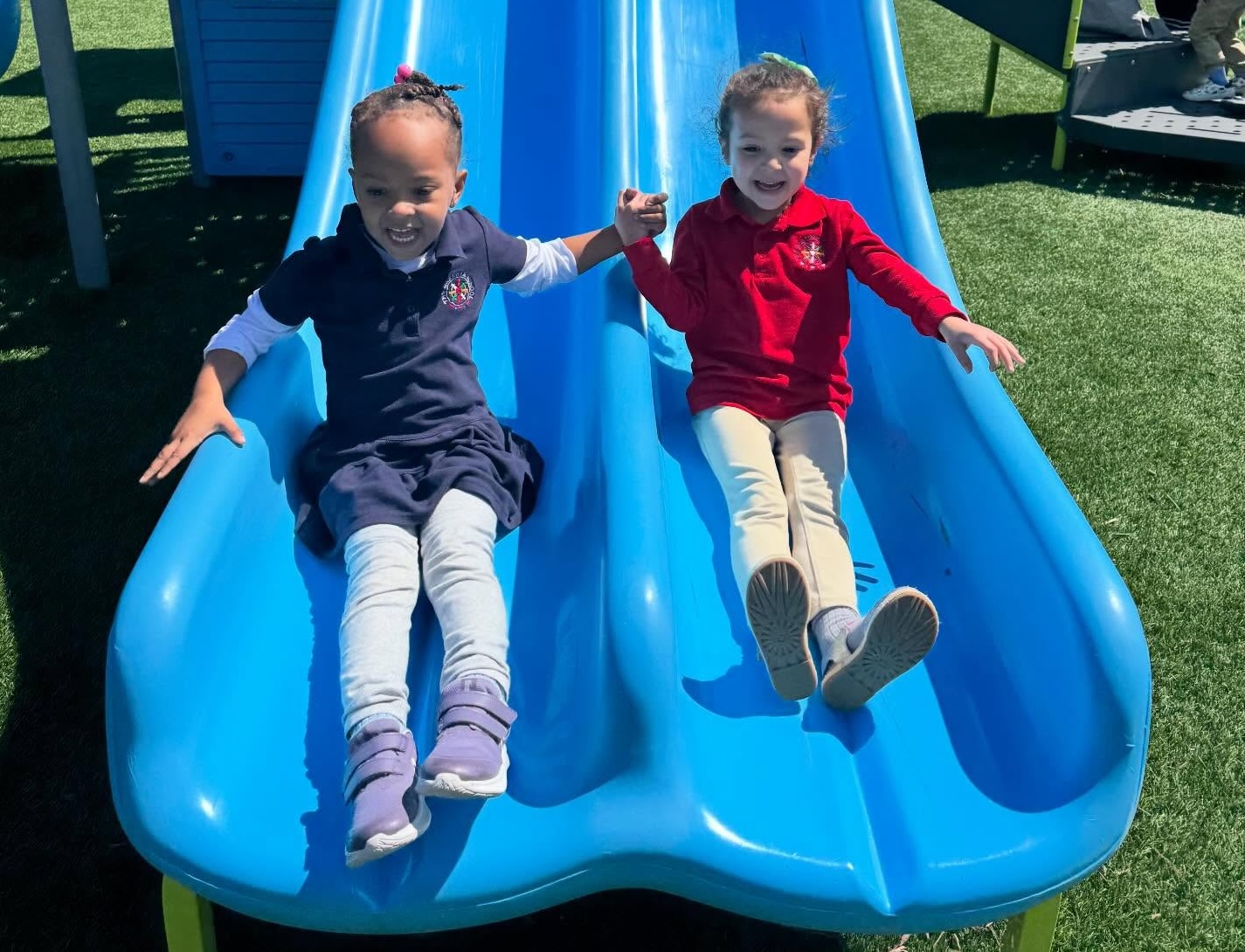 two young female students coming down the slide on playground