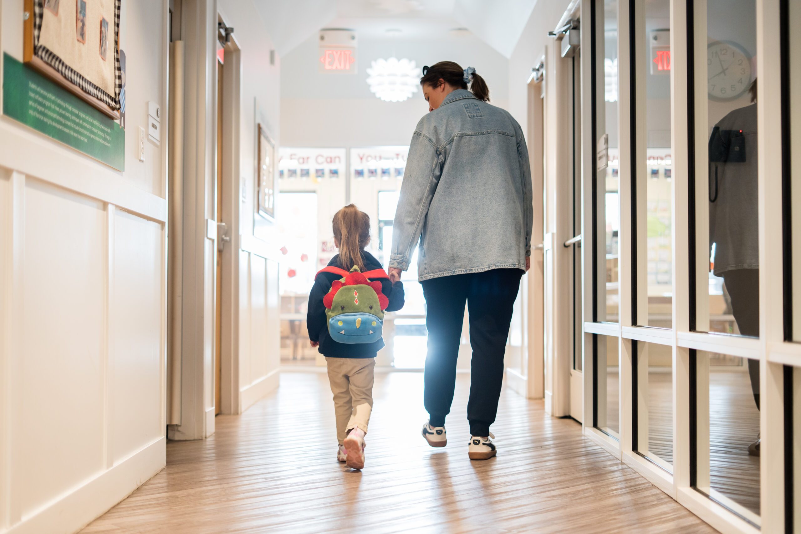 Child walking through the hallway at school with backpack and holing hands with an adult